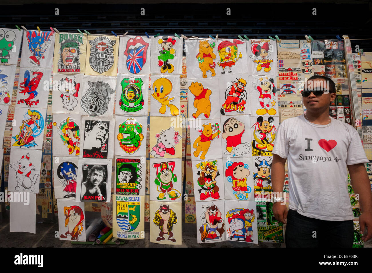 A vendor wearing 'I love Sriwijaya Air' t-shirt waiting for customers at a roadside shop of fictional character stickers in Surabaya, Indonesia. Stock Photo