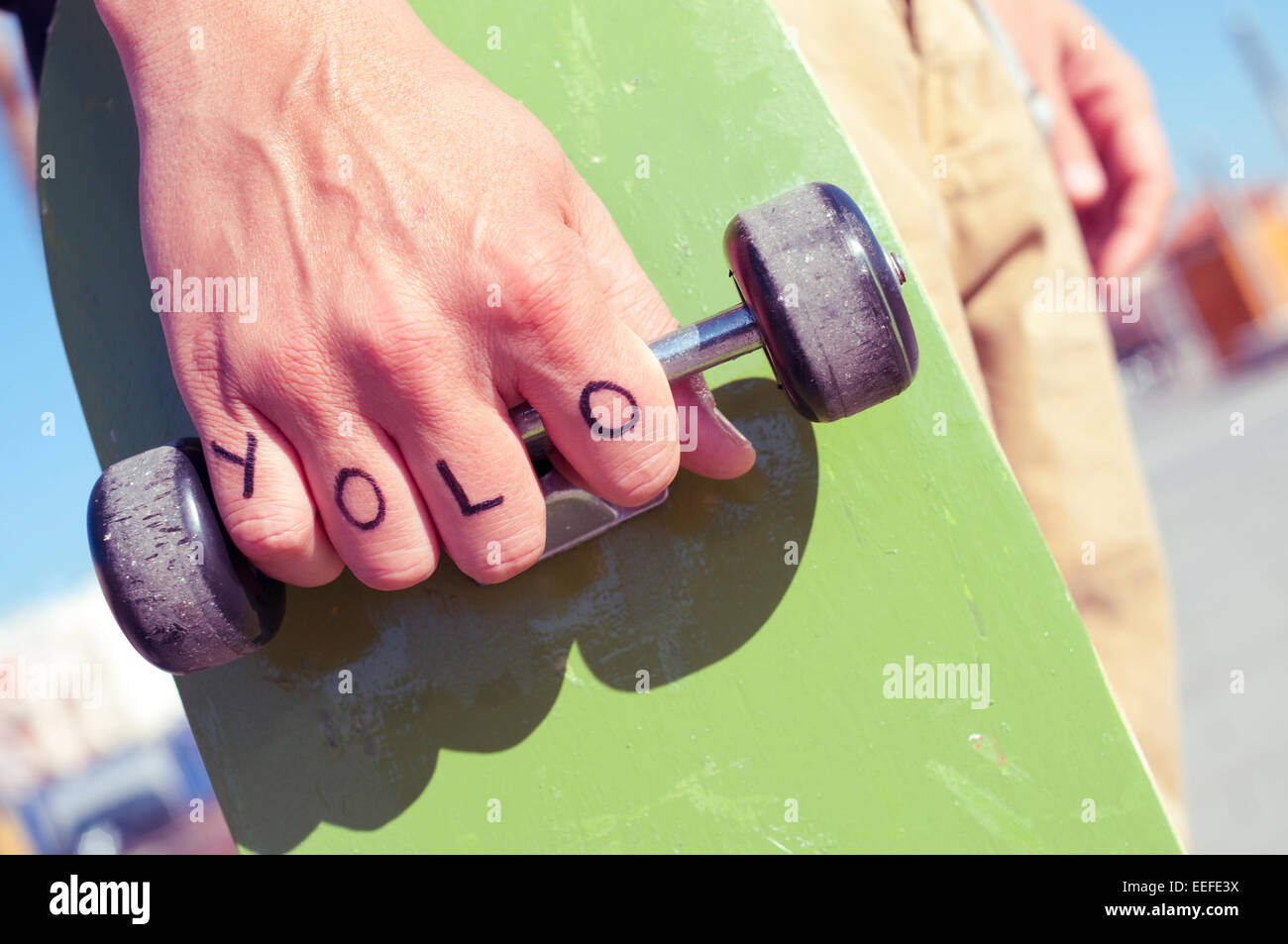 closeup of a young man with the word yolo, for you only live once, tattooed in his hand holds a skateboard Stock Photo