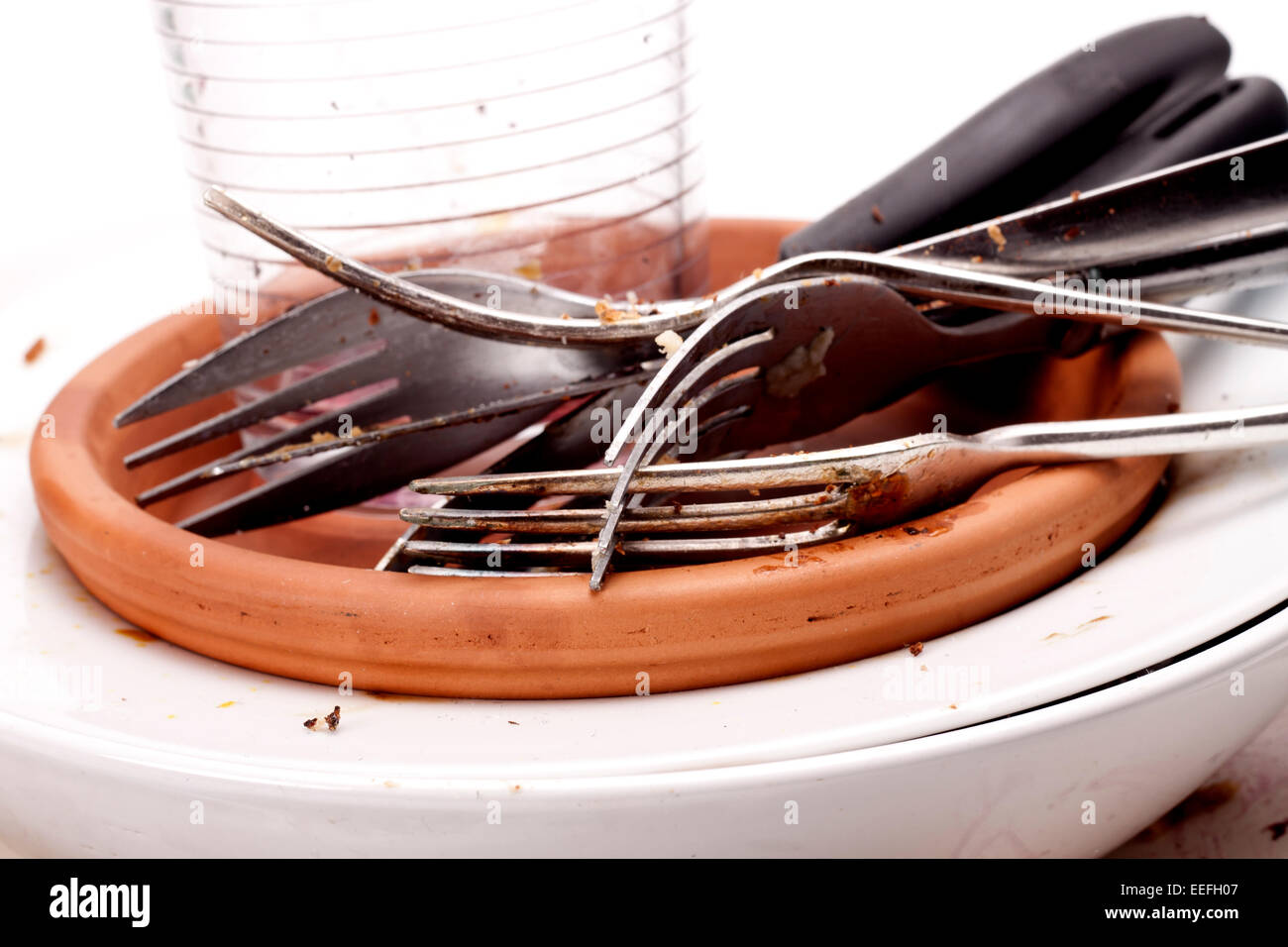 A stack of dirty plates, forks, knifes and a glass that needs washing-up. Stock Photo