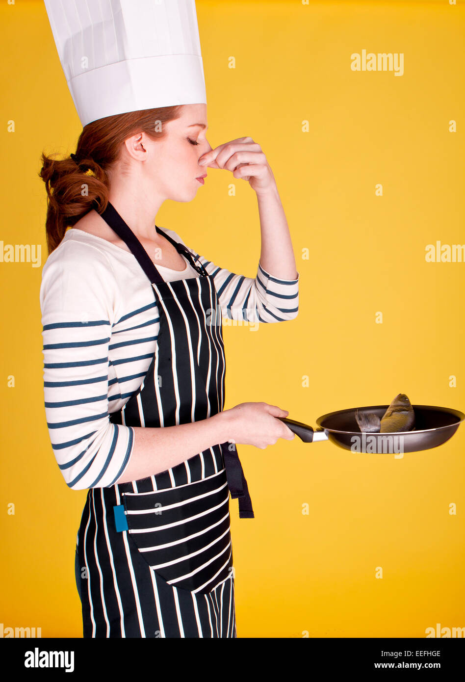 A young female cook holding her nose to block out the smell of fresh raw fish. Stock Photo