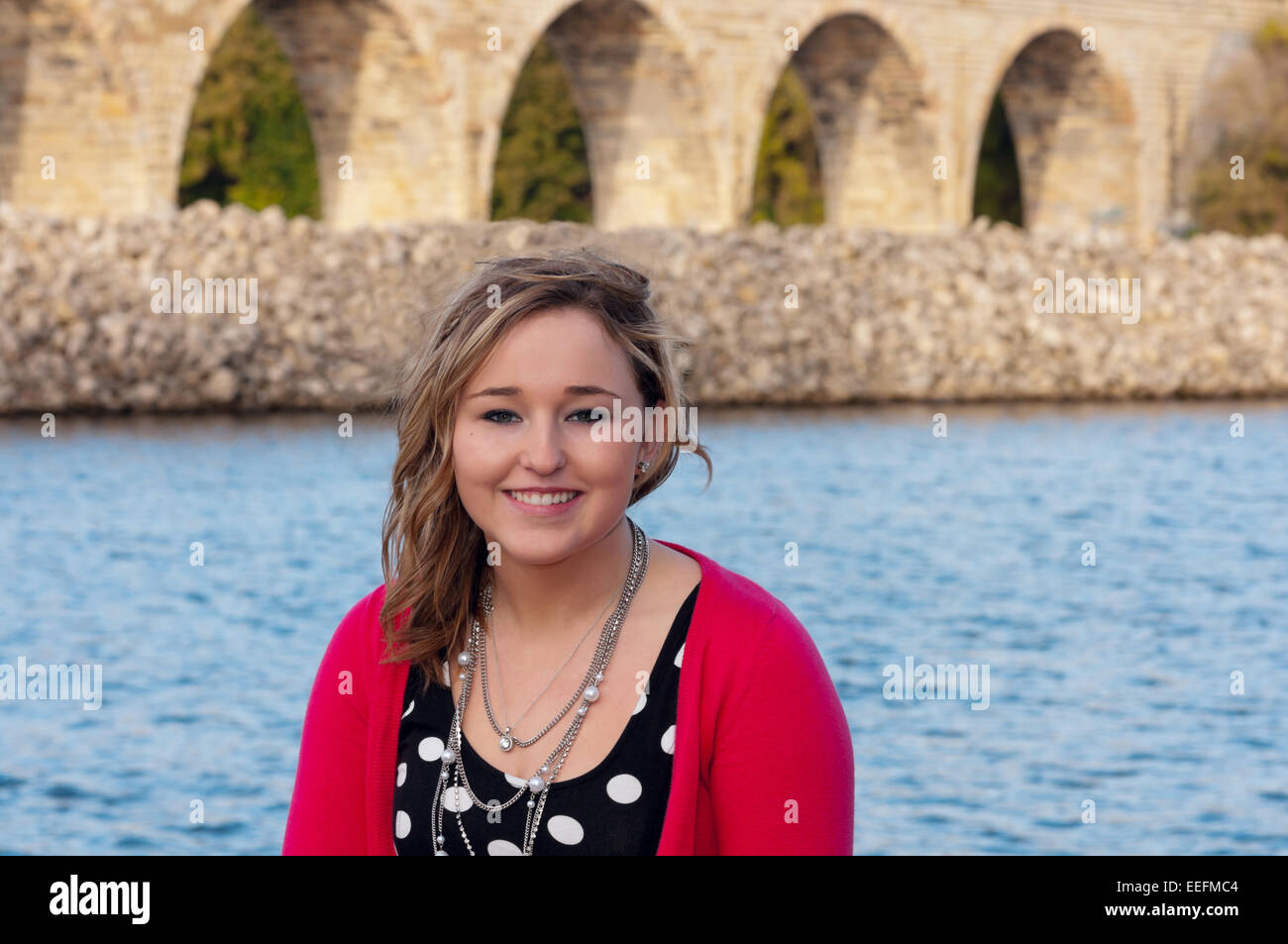 Outdoor head and shoulders portrait of young adult or teen female smiling with stone arch bridge of minneapolis in background Stock Photo