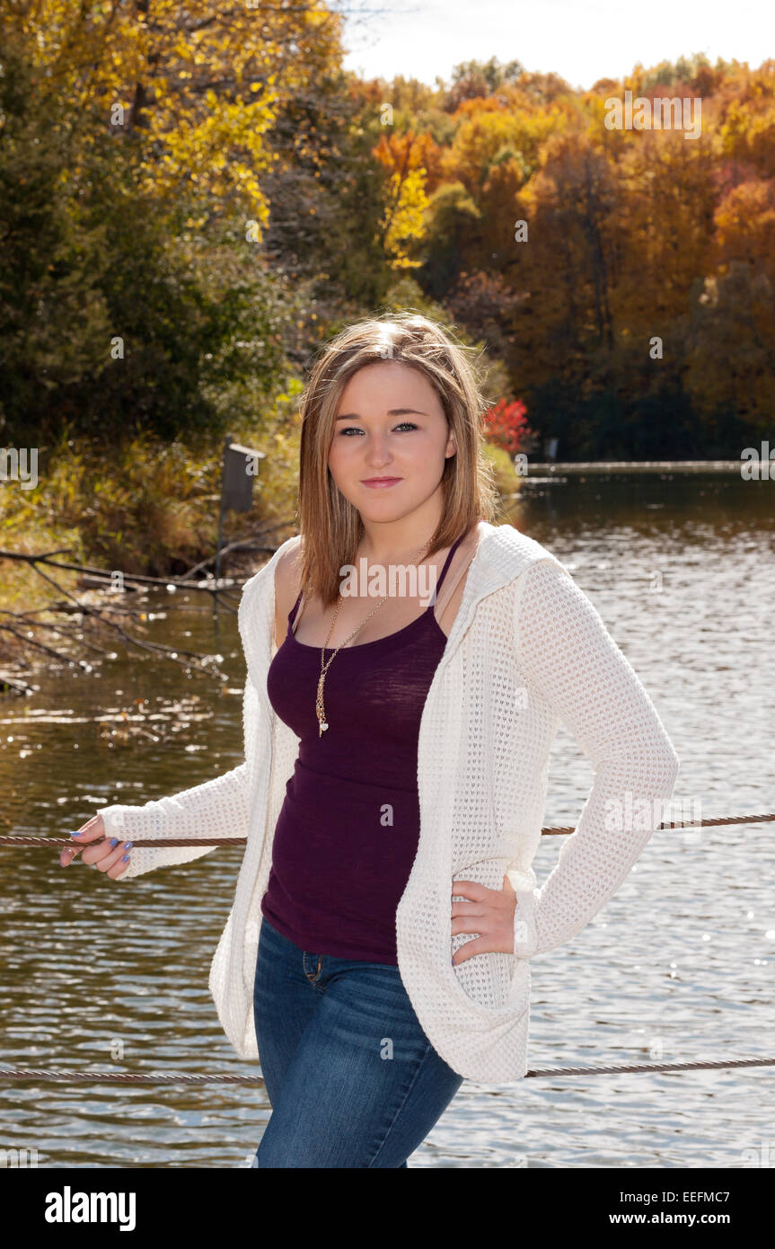 Young adult female standing on lake pier with golden colors of autumn in background Stock Photo