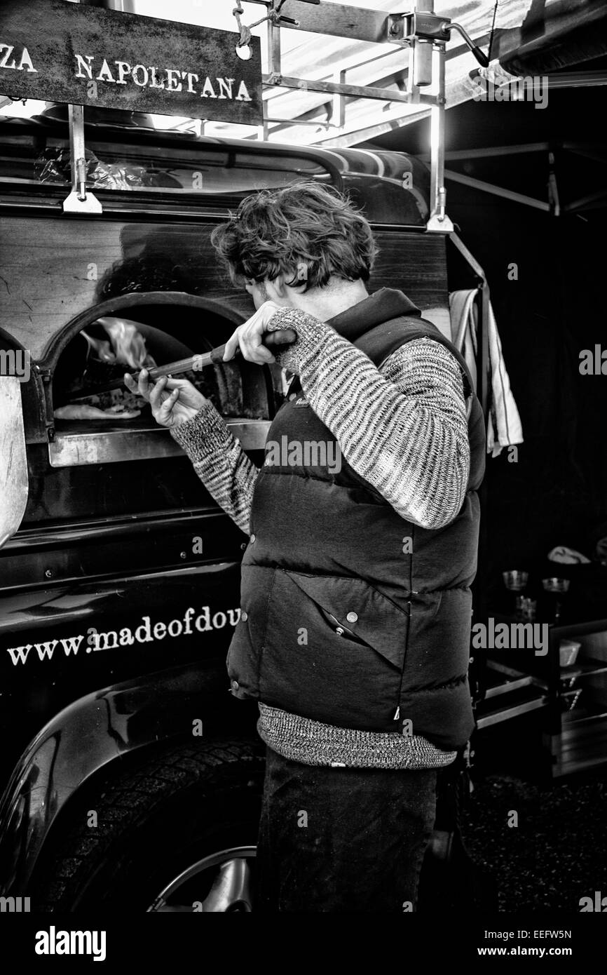 Market stallholder tends a pizza oven, Jimmy's Farm, Ipswich, Suffolk, UK Stock Photo