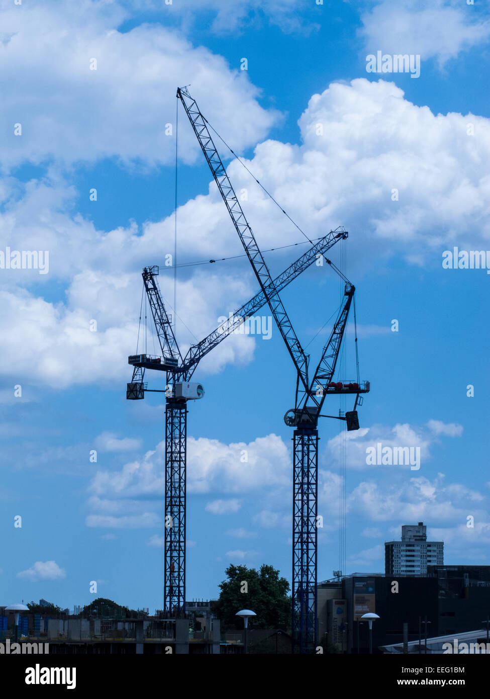 Cranes in a construction site silhouetted against blue skies and white ...