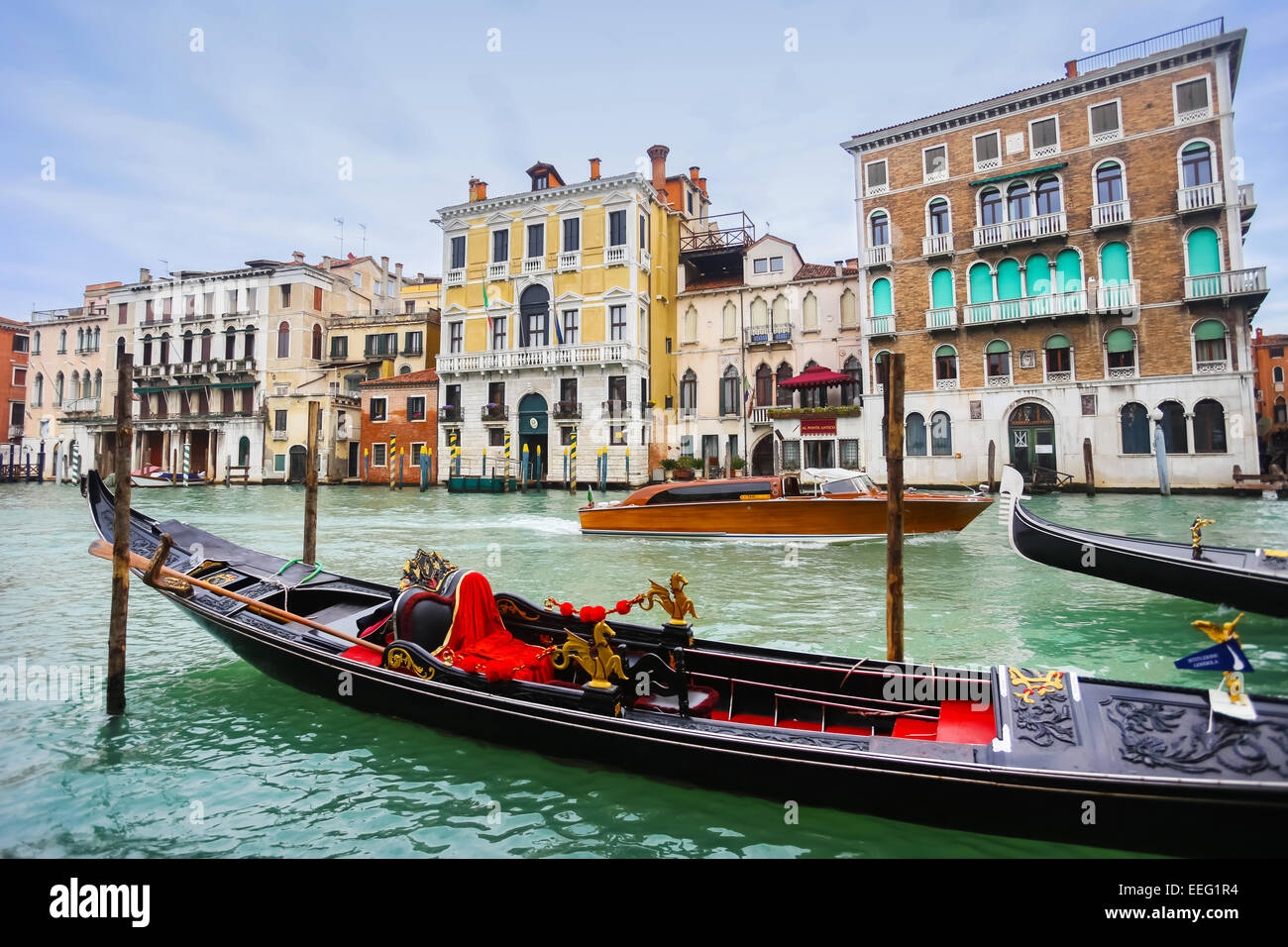 Empty gondola parked in a Campo Erberia square on grand canal with gondolas and boats passing behind it in Venice, Italy. Stock Photo