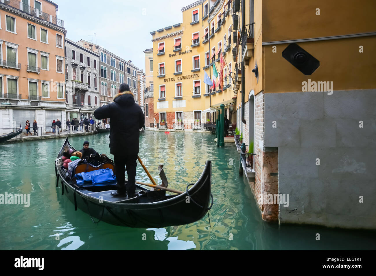 Tourists sailing in a gondola through a water canal next to Hotel Cavalletto in Venice, Italy. Stock Photo
