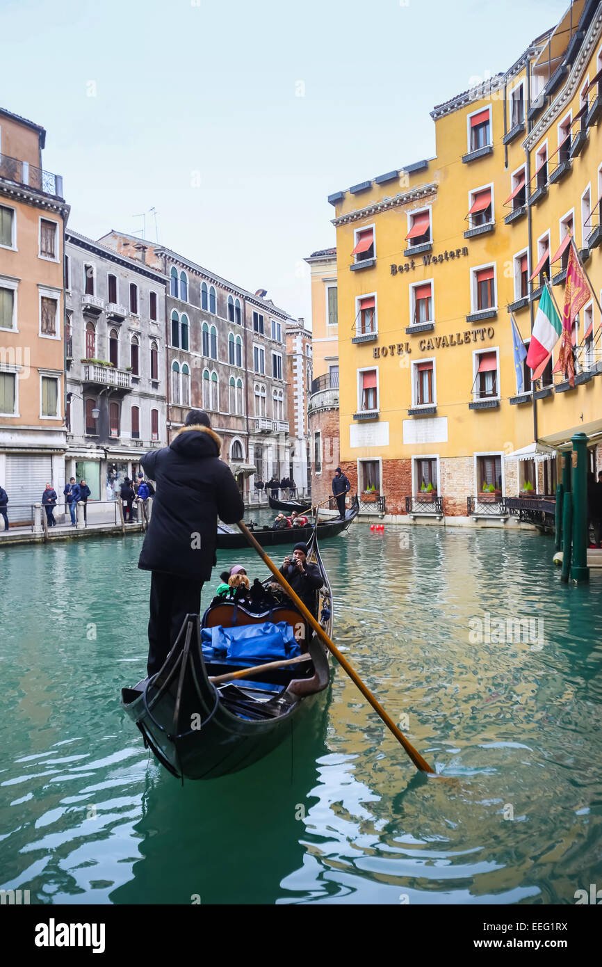 Tourists sailing in a gondola through a water canal next to Hotel Cavalletto in Venice, Italy. Stock Photo