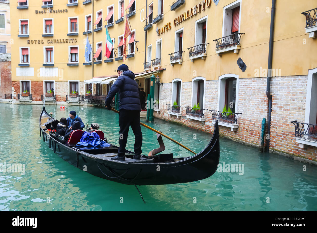 Tourists sailing in a gondola through a water canal next to Hotel Cavalletto in Venice, Italy. Stock Photo