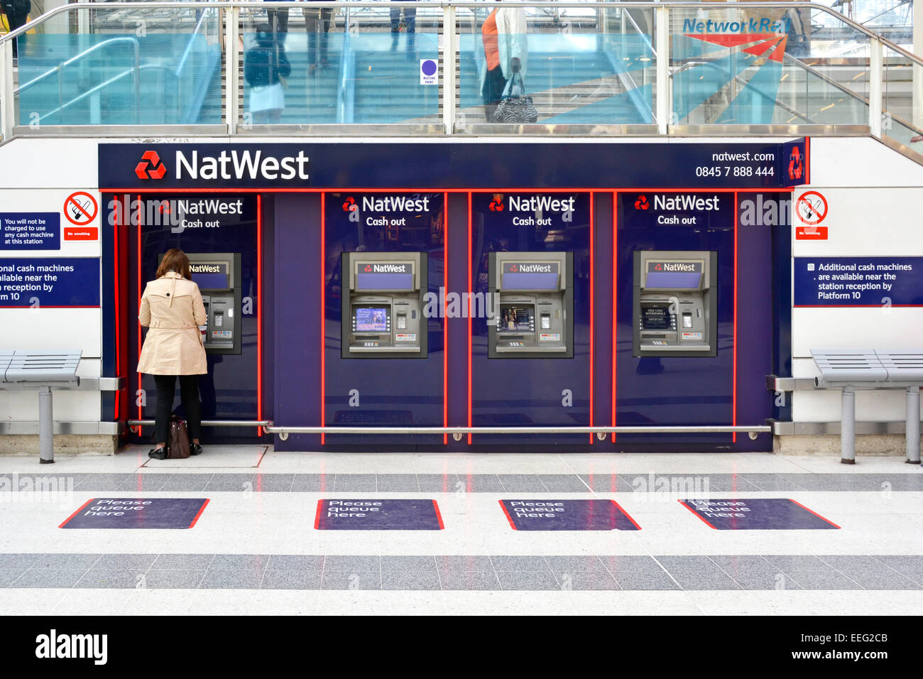 Nat West bank back view woman drawing cash from out atm machines on the main passenger concourse at London Liverpool Street train station England UK Stock Photo