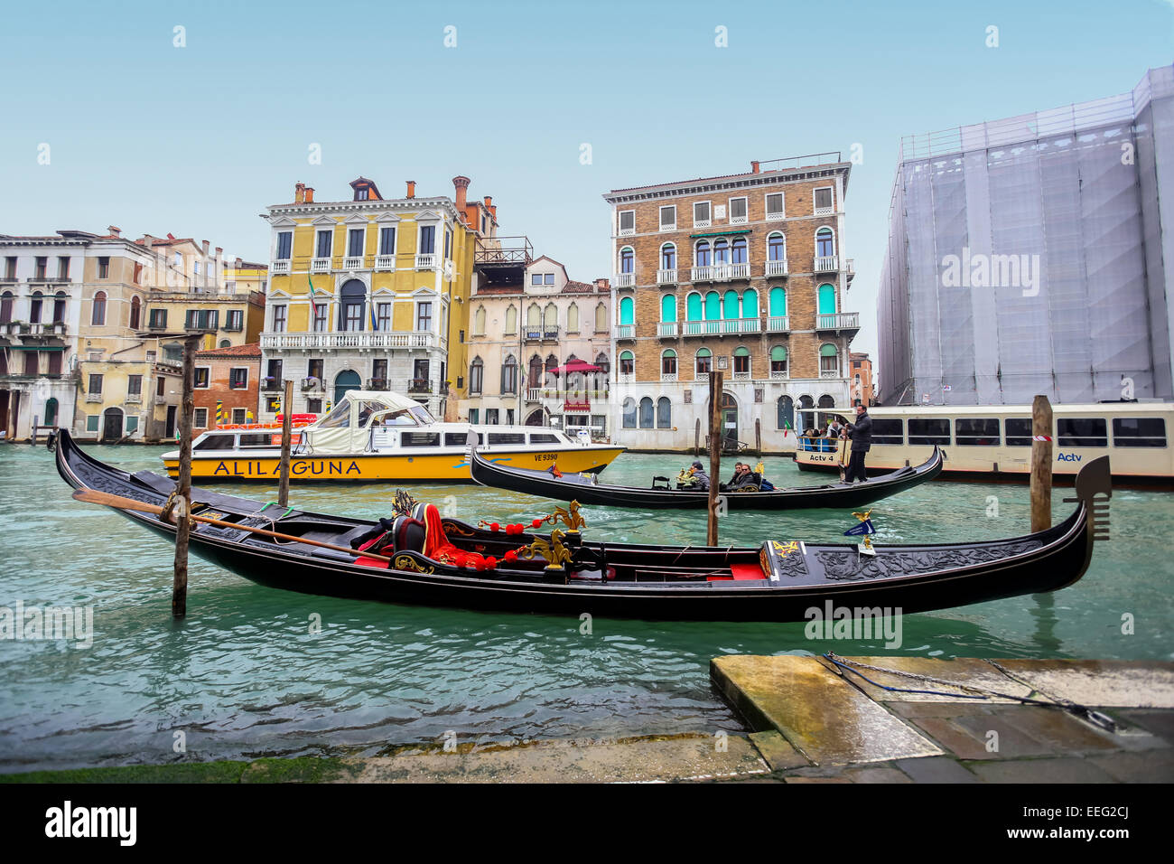 Empty gondola parked in a Campo Erberia square on grand canal with gondolas and boats with tourists passing behind in Venice. Stock Photo