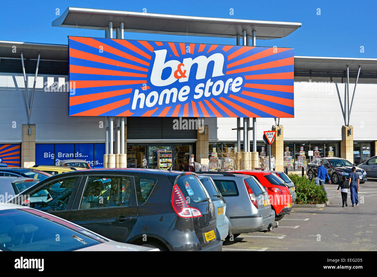 Shoppers at B&M Retail Ltd home bargains store business sign & entrance beyond busy free car parking at Lakeside retail park Thurrock Essex England UK Stock Photo