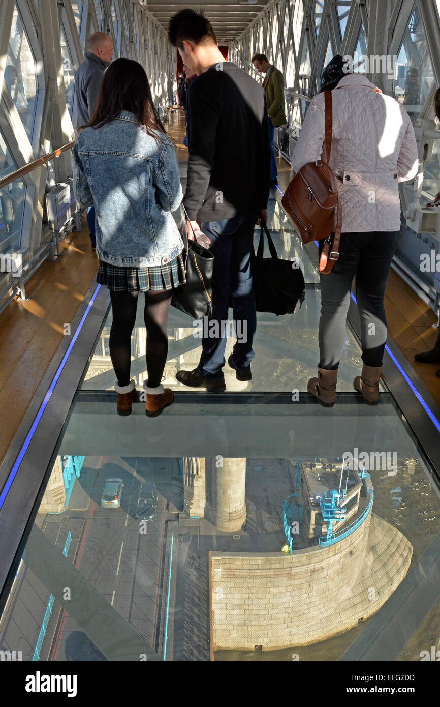 Visitors and tourists standing on glass floor on Tower Bridge high level walkway with bridge & road traffic and river thames below London England UK Stock Photo