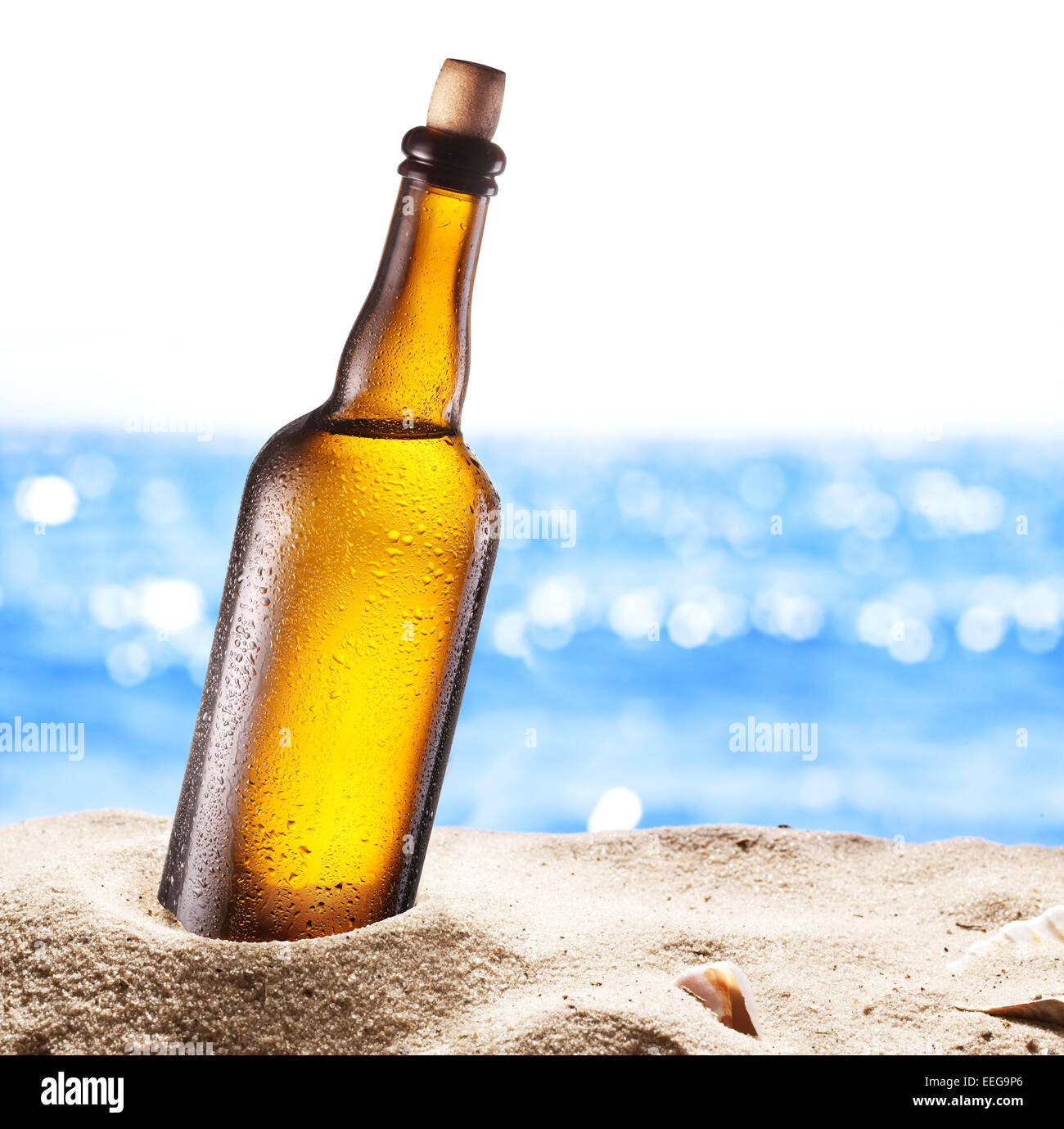 Photo of cold beer bottle in the sand. Sparkling sea at the background. Stock Photo