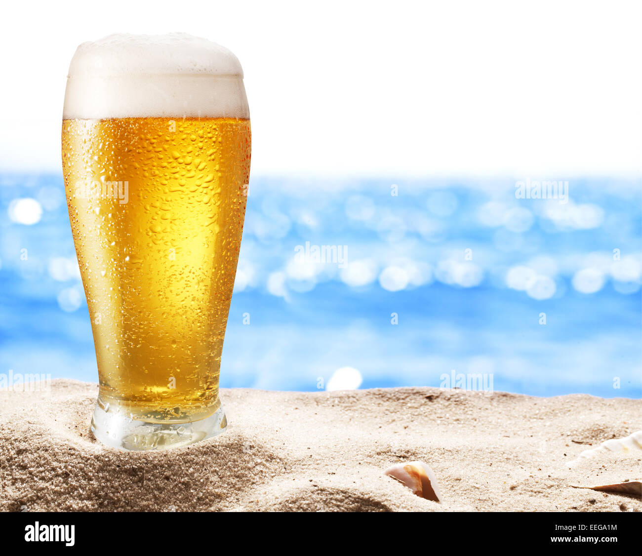 Photo of cold beer botle in the sand. Sparkling sea at the background. Stock Photo
