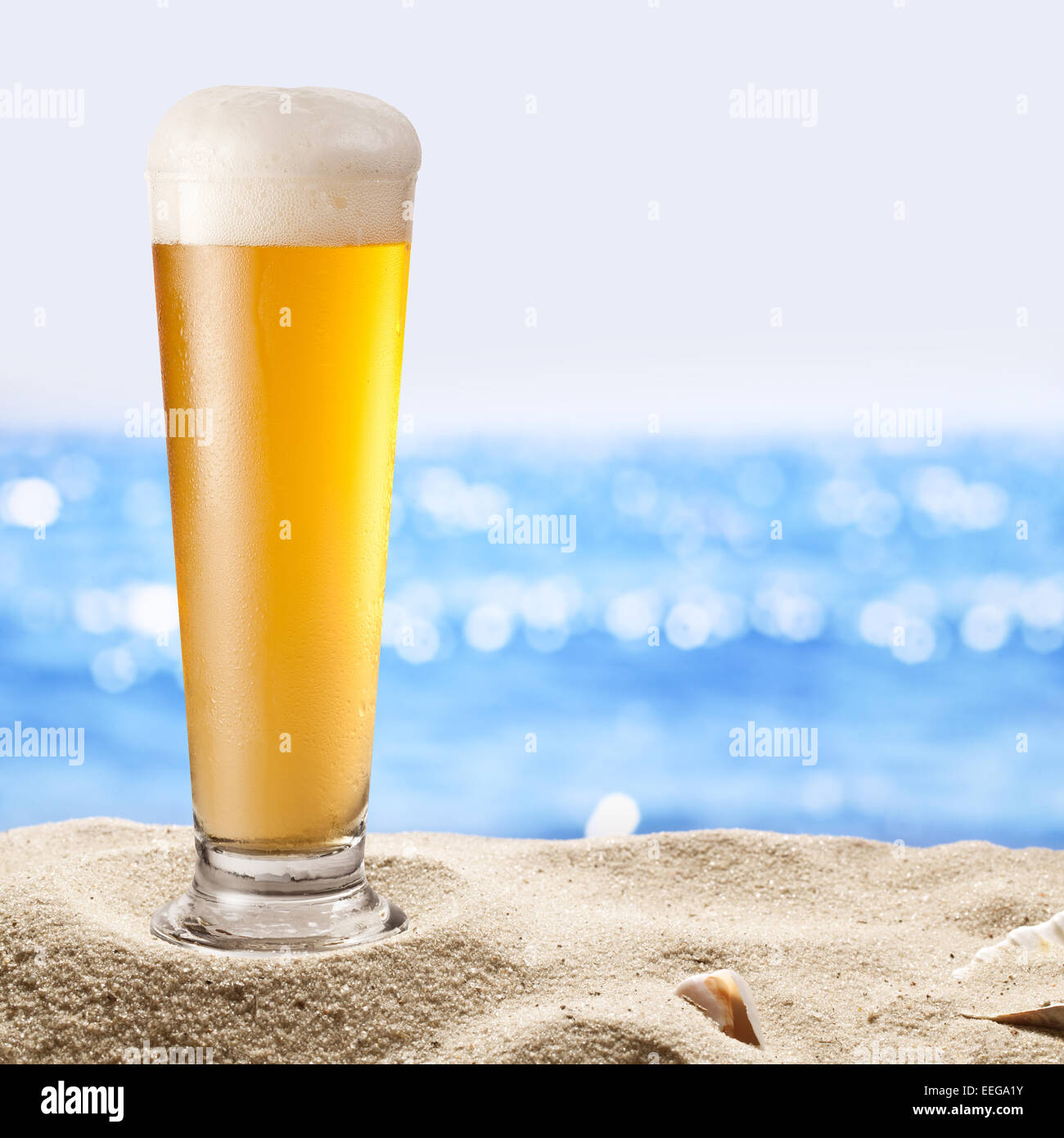 Photo of cold  glass of beer in the sand. Sparkling sea at the background. Stock Photo
