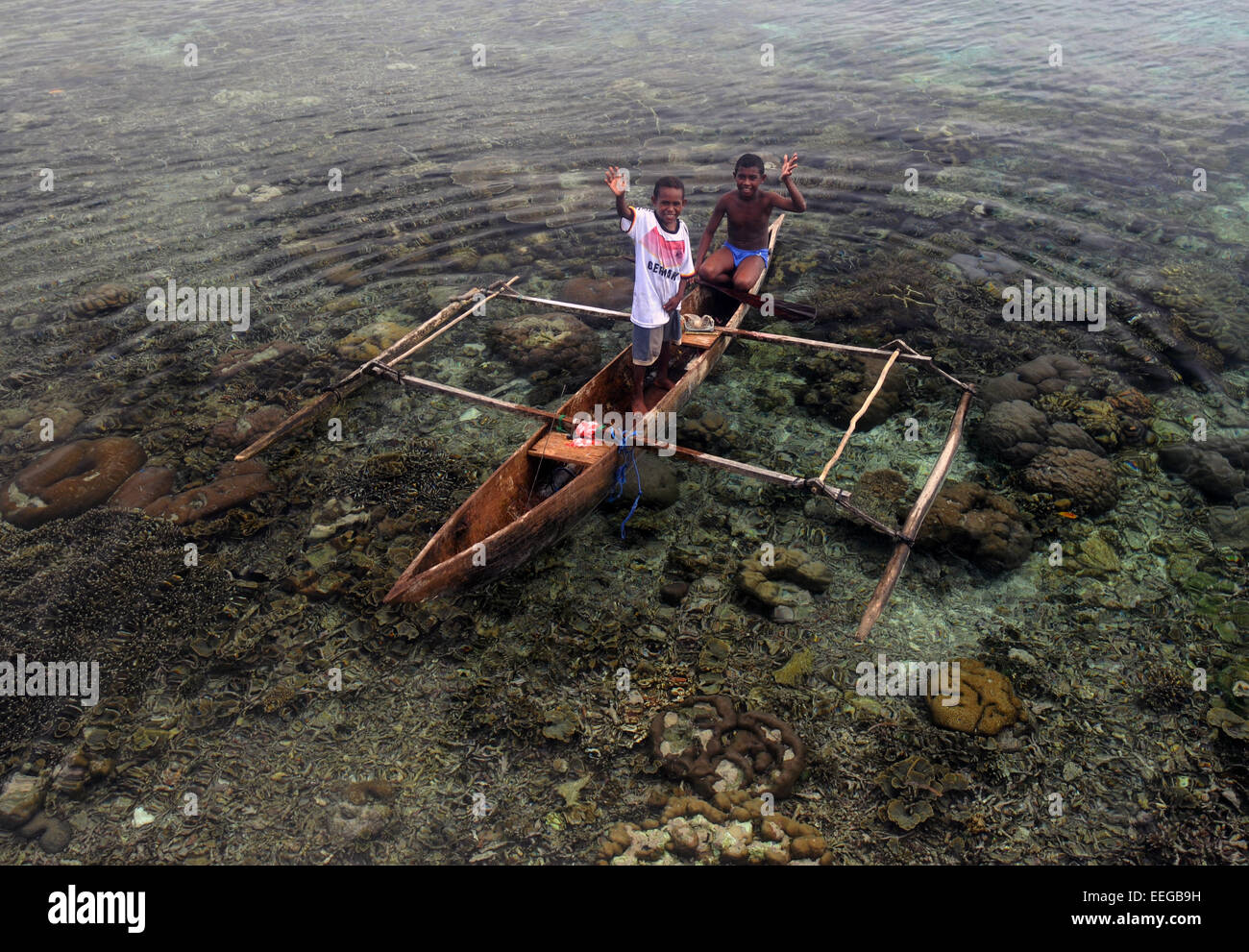 Kids waving from tiny old dugout canoe, Gam Island, Raja Ampat, Papua province, Indonesia. No MR Stock Photo