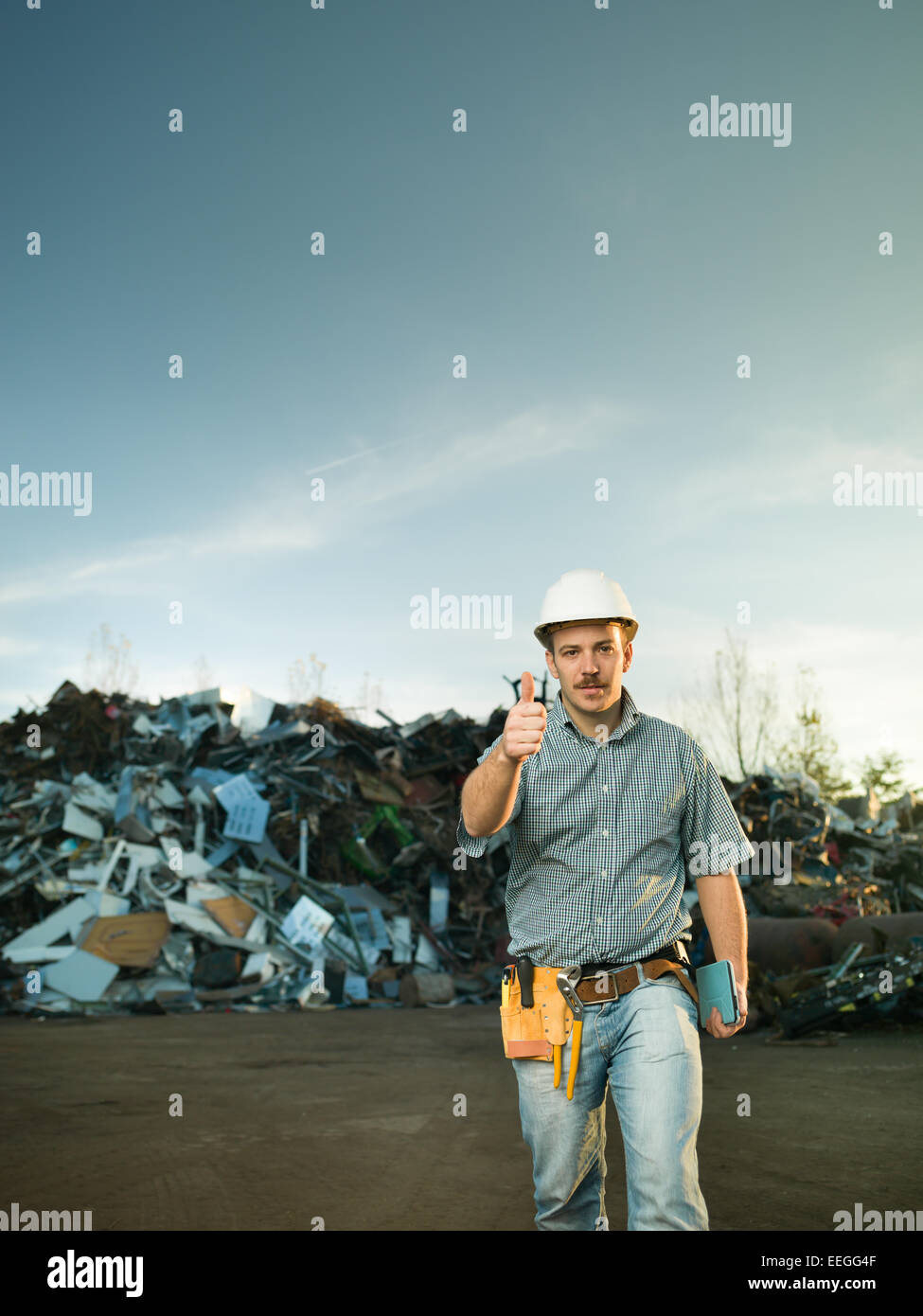 portrait of young caucasian engineer holding thumb up in scrap metal landfill outdoors. copy space available Stock Photo