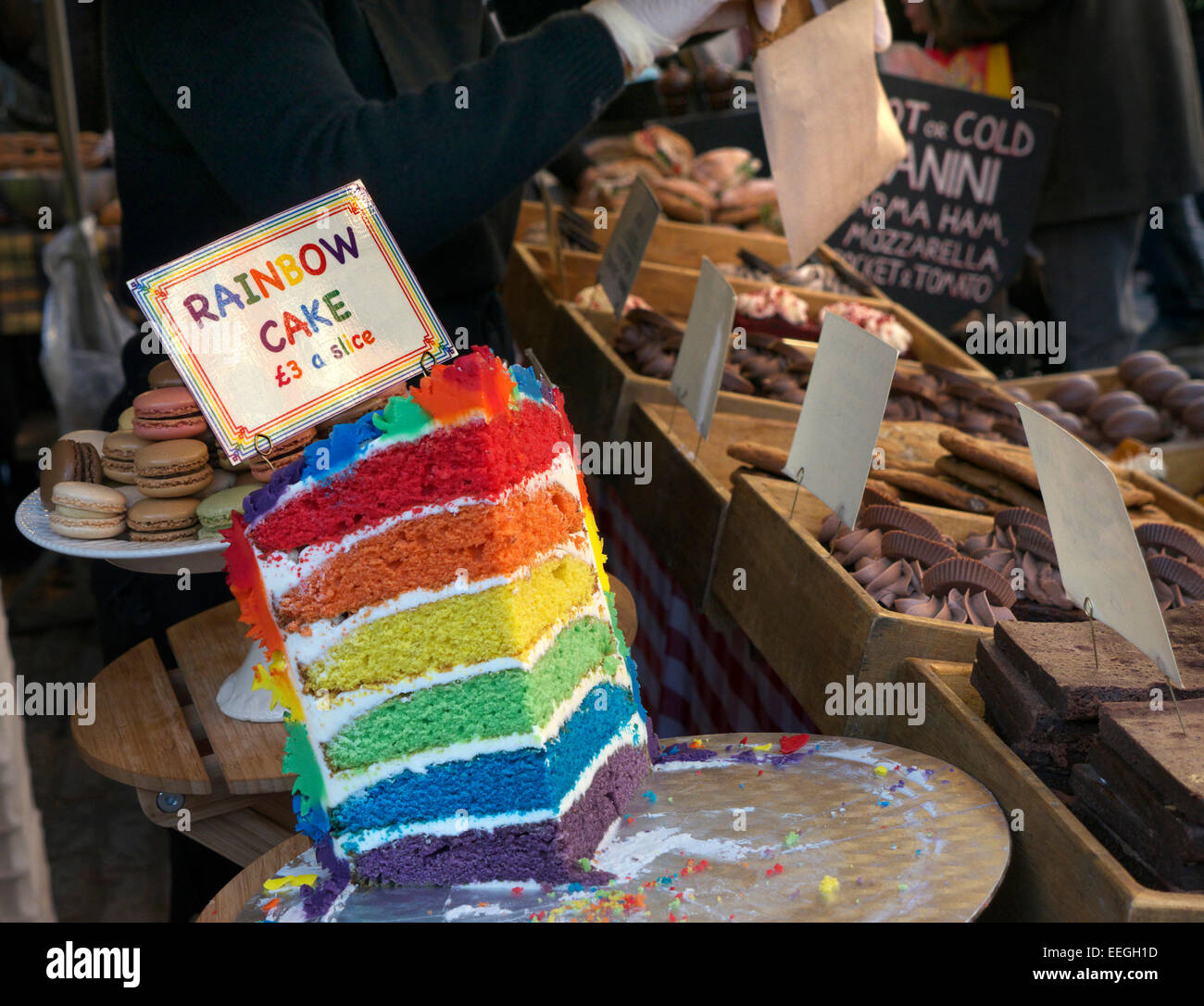 Rainbow layer cake display outdoor market stall on sale at Covent Garden piazza street food market stall London UK Stock Photo