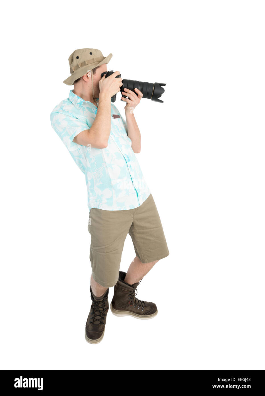 Silly man tourist in blue shirt, brown shorts and hat holding big dslr camera and shooting. Traveler concentrating and making pi Stock Photo
