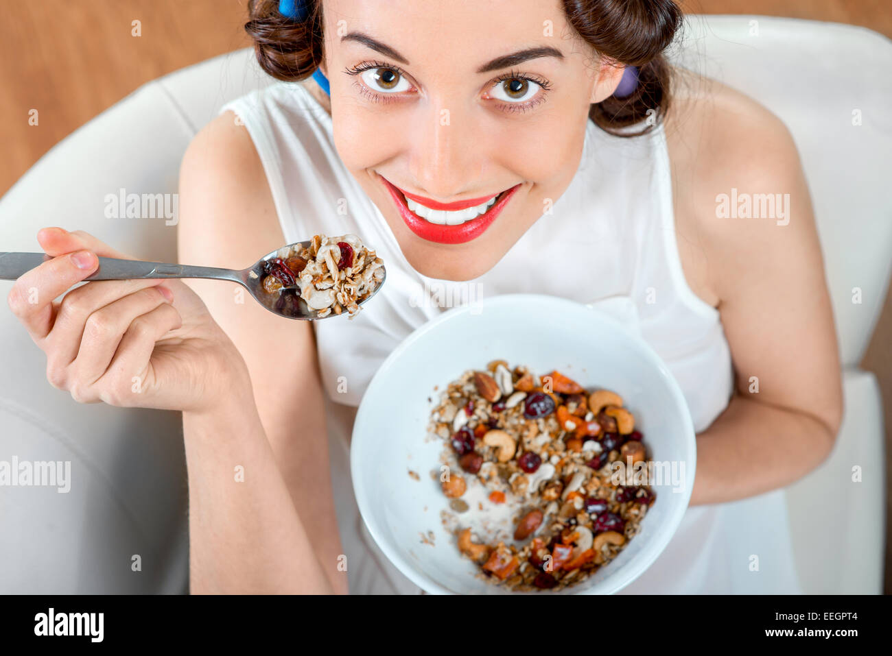 Young Woman With Hair Curlers Eating Granola Breakfast Sitting On