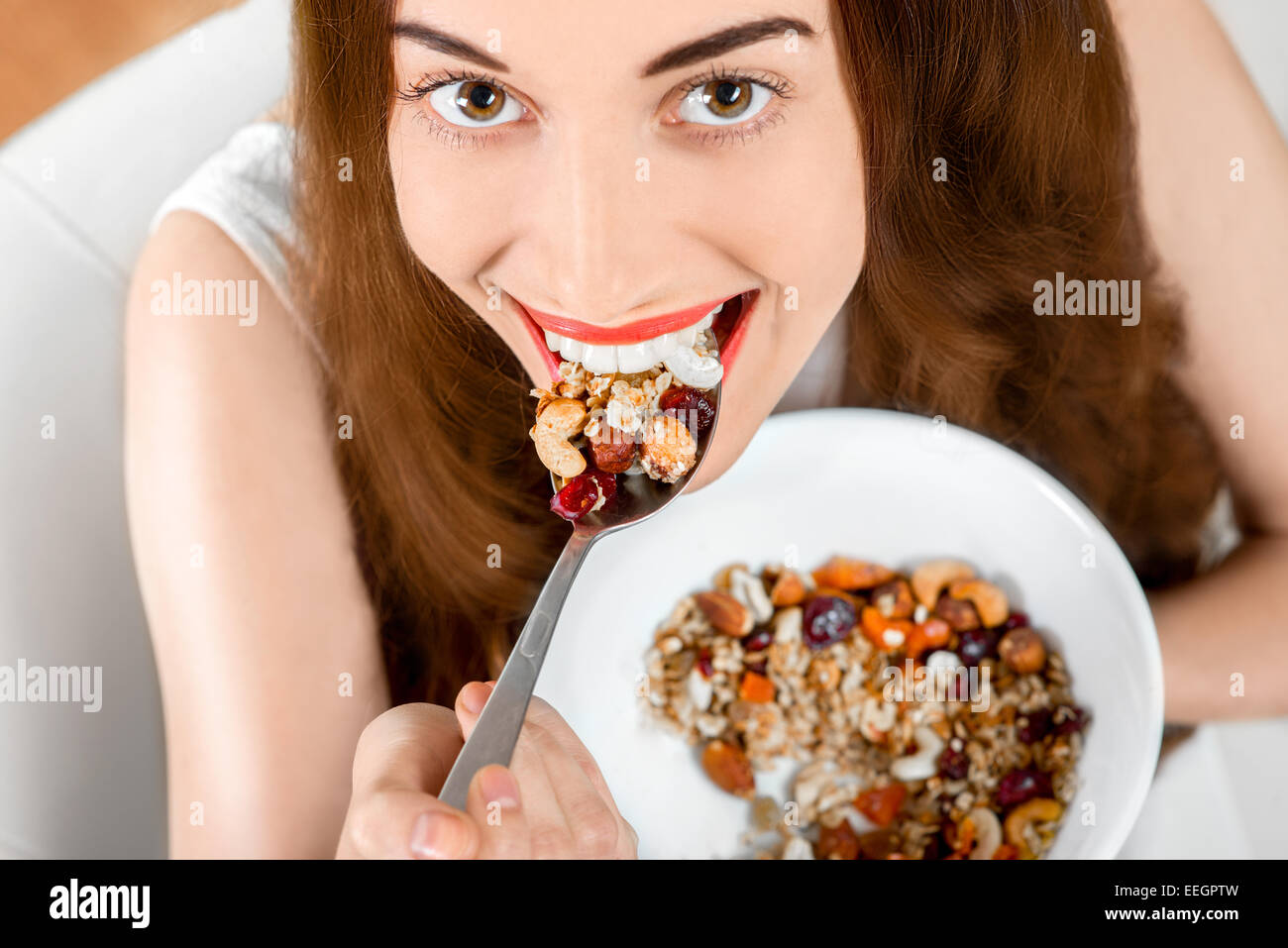 Young positive woman eating granola breakfast on the couch at home. Up