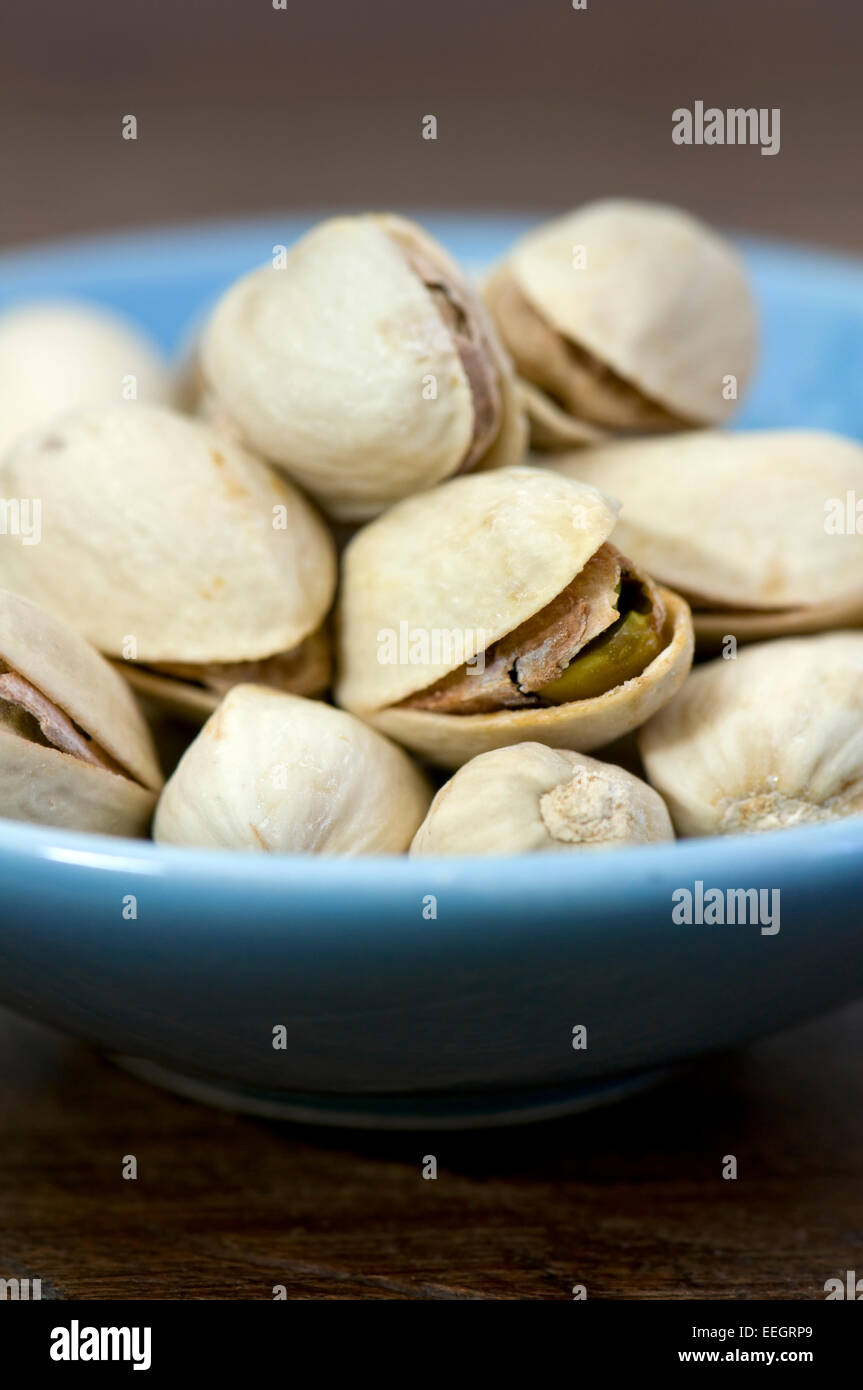Small blue bowl of pistachio nuts on dark background Stock Photo