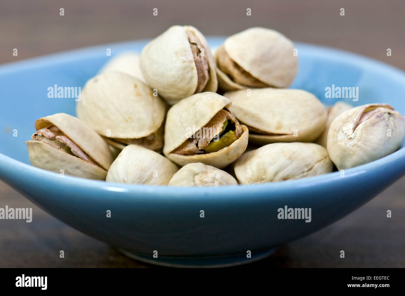 Small blue bowl of pistachio nuts on dark background Stock Photo