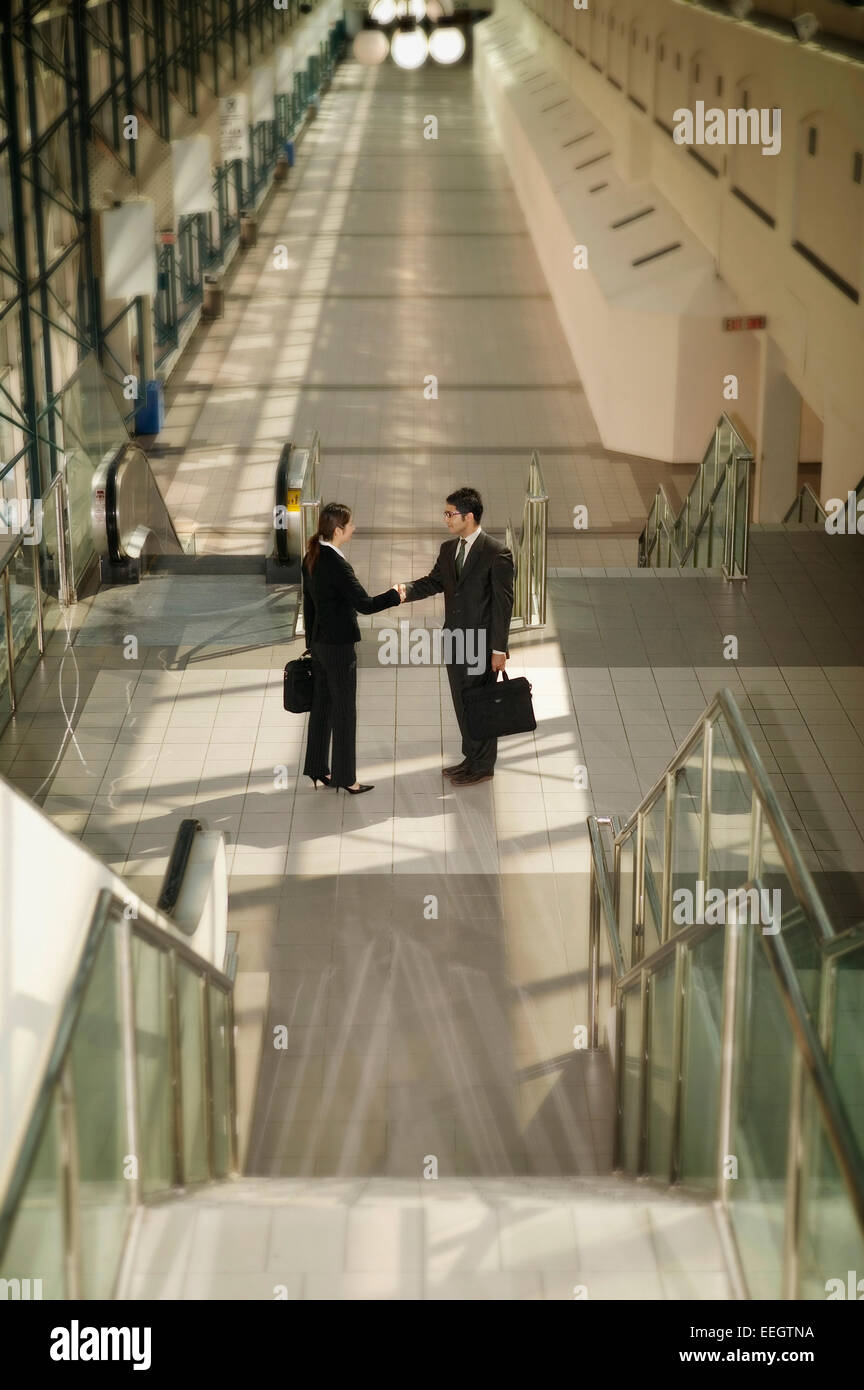 Business couple shaking hands at the bottom of stairs Stock Photo