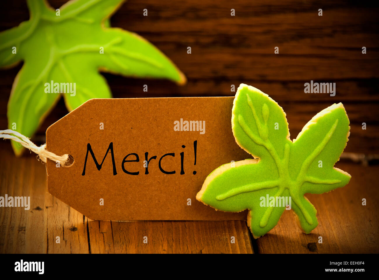 Brown Organic Label With French Text Merci On Wooden Background With Two Leaf Cookies And Frame Stock Photo