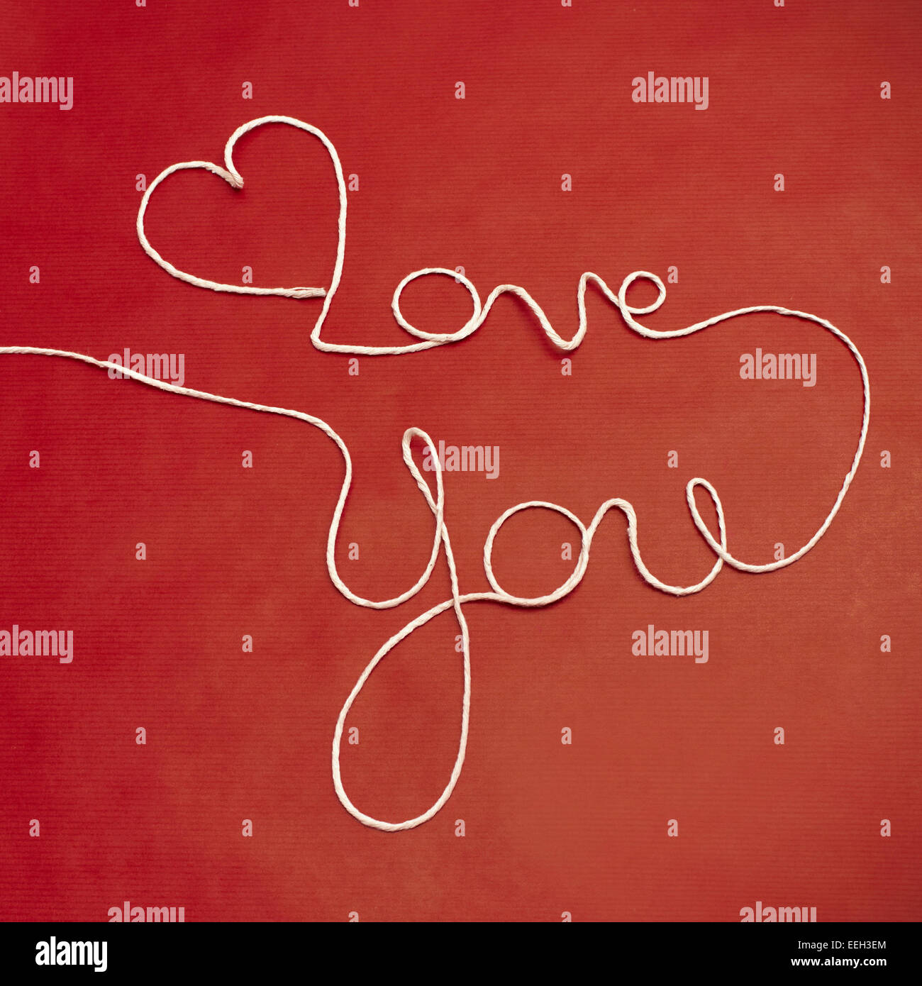 Love You words and heart symbol made of white twine on red background