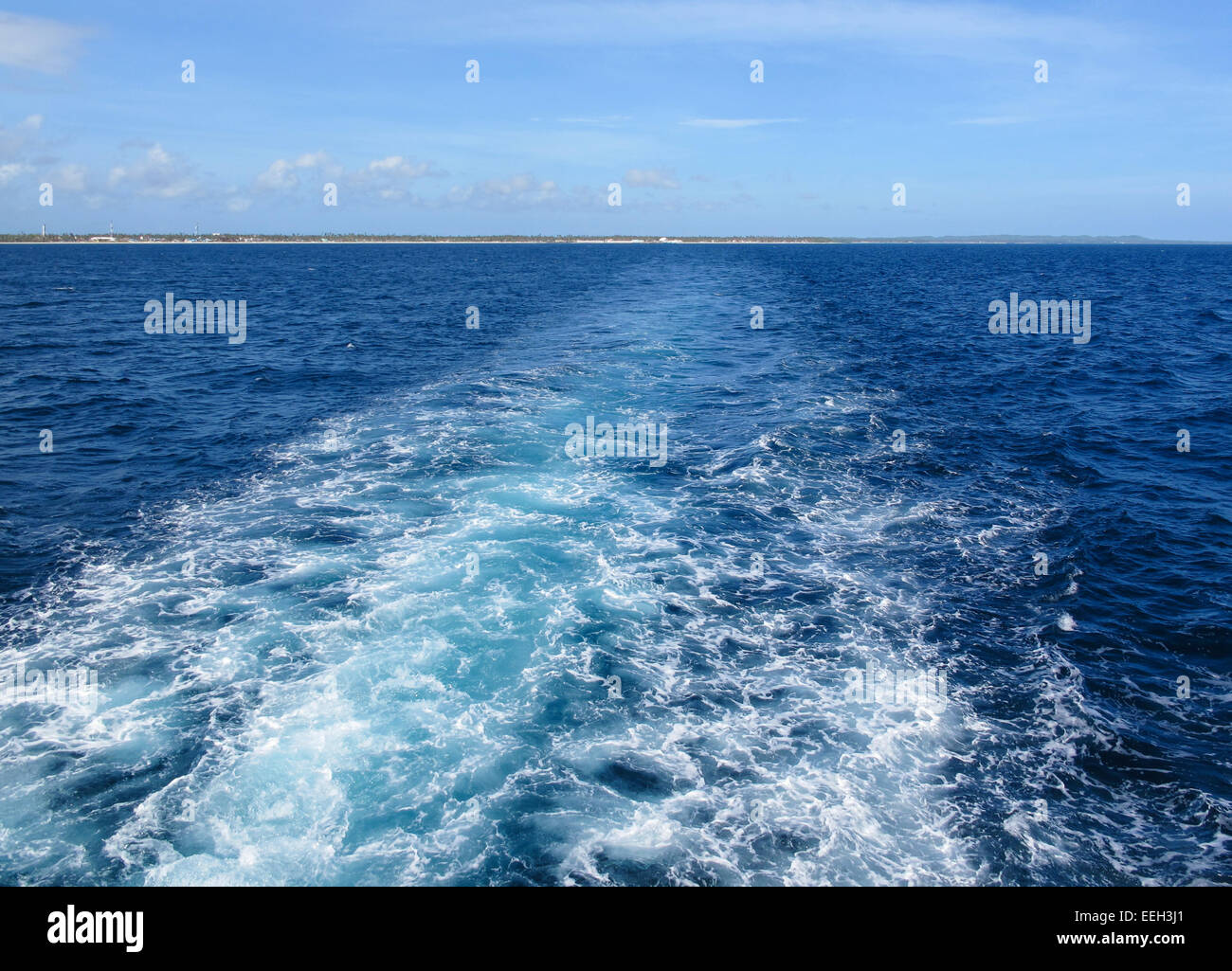 Ship or boat wake in a tropical sea looking back at a tropical holiday island - concept of departure or going home Stock Photo
