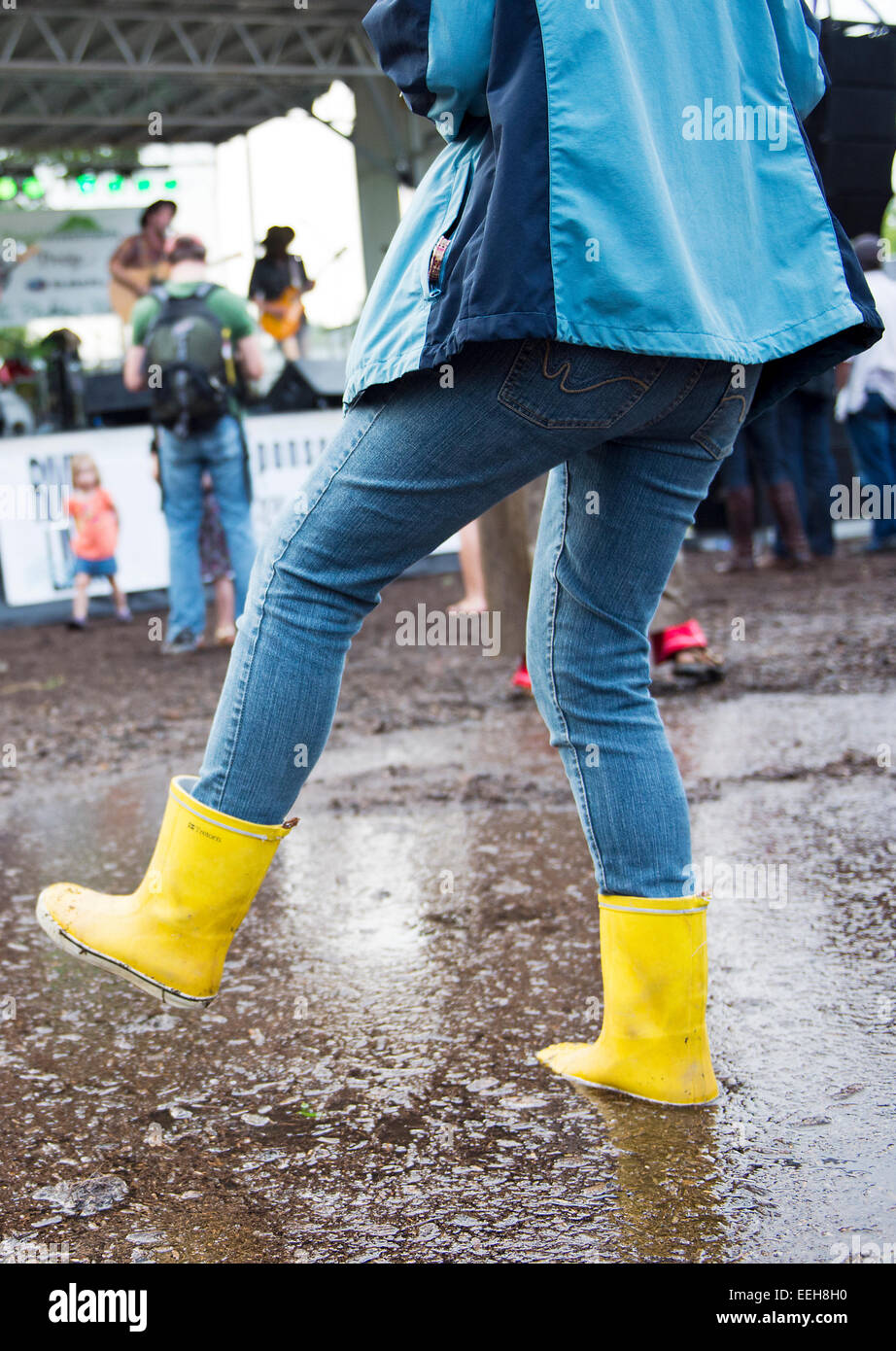 Woman wearing yellow rain boots at 'River Fest' splashing in puddle after a rain storm in Asheville NC Stock Photo