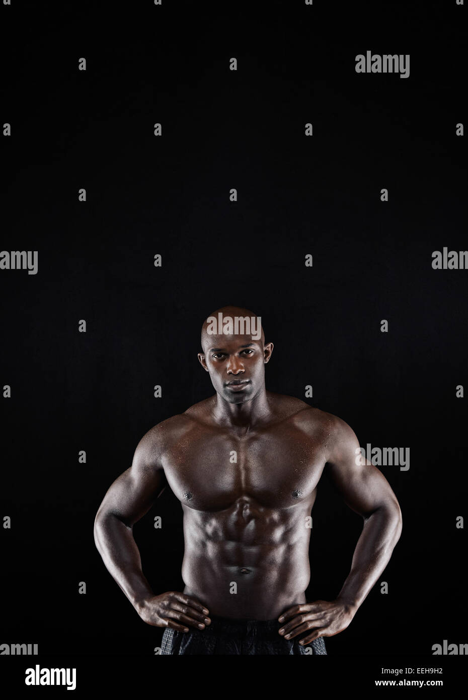 Studio shot of muscular man posing with his hands on hips against black