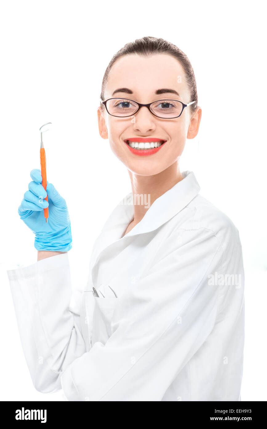 Young woman doctor holding dental mirror and looking at camera on white