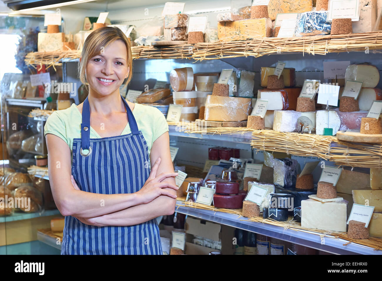 Owner Of Delicatessen Standing Next To Cheese Display Stock Photo