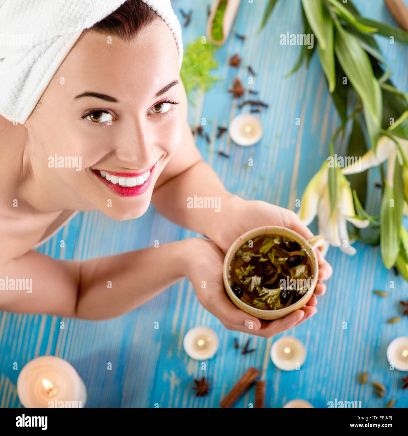 Smiling young woman with cup of herbal tea in bath towel in spa salon. Herbal treatment. Stock Photo