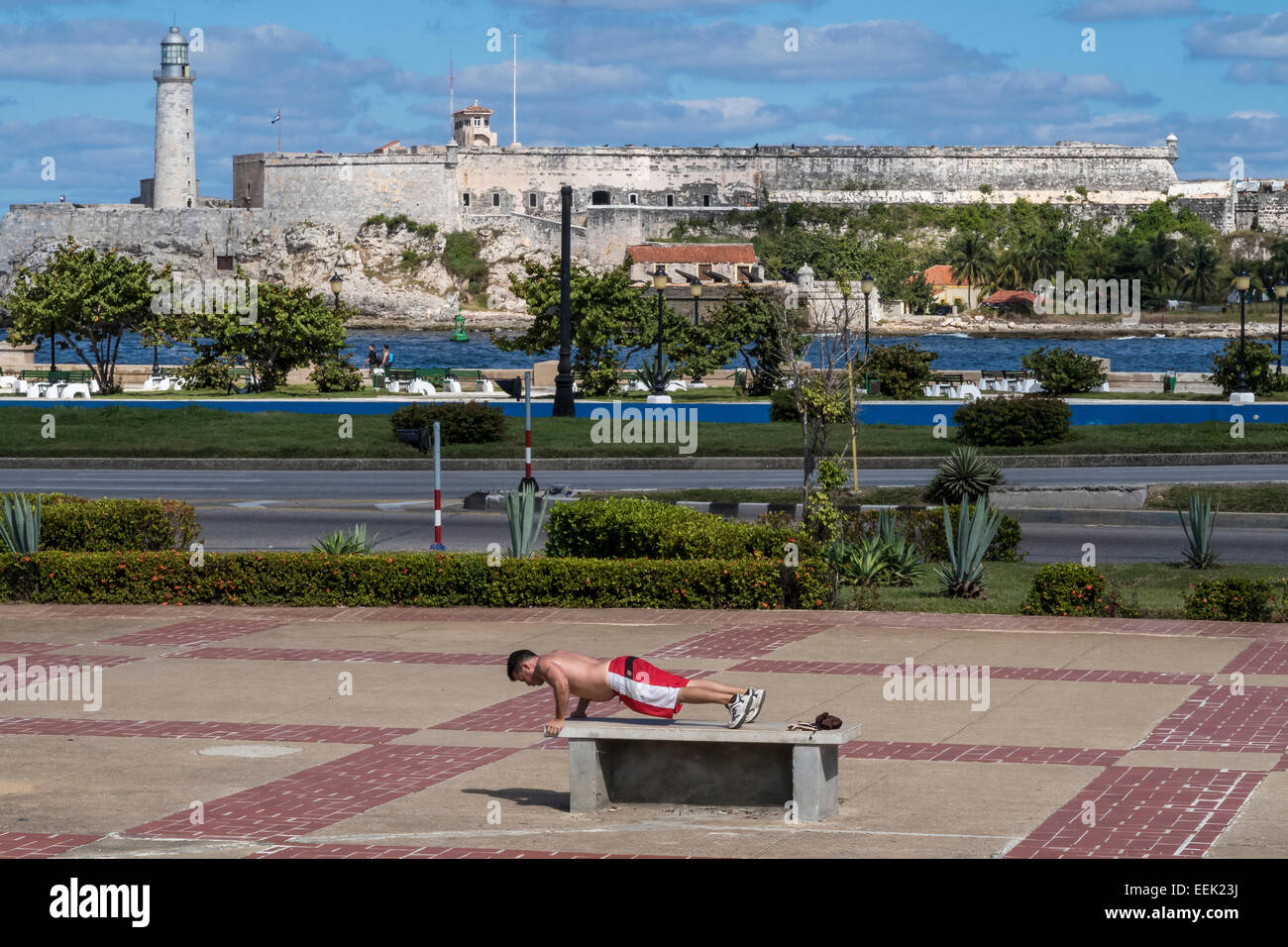 Young man exercises at the Parque Martires del 71, with the Castillo del Morro beyond the bay. Havana, Cuba. Stock Photo