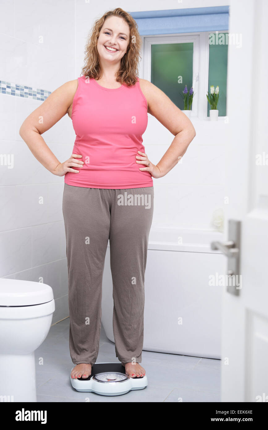 Happy Woman Weighing Herself On Scales In Bathroom Stock Photo