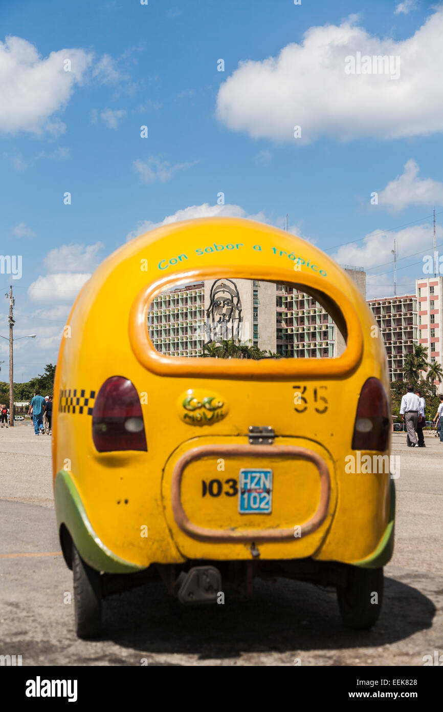 Yellow coco taxi cab parked at the Ministry of Interior building with image of Che Guevara in Plaza de la Revolución, Havana, Cuba Stock Photo