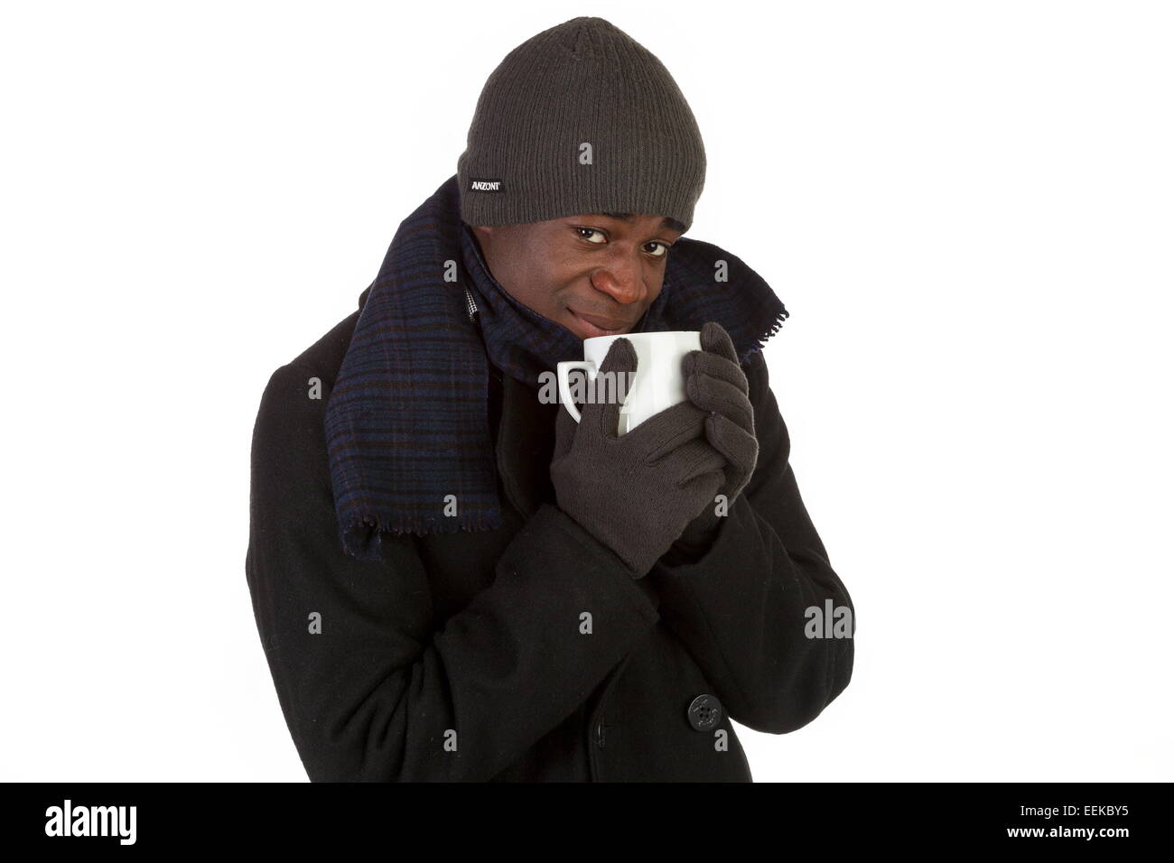Junger dunkelhäutiger Mann erklätet, im Wintermantel mit Schal, Handschuhen und Mütze, trinkt eine warme Tasse Tee Stock Photo