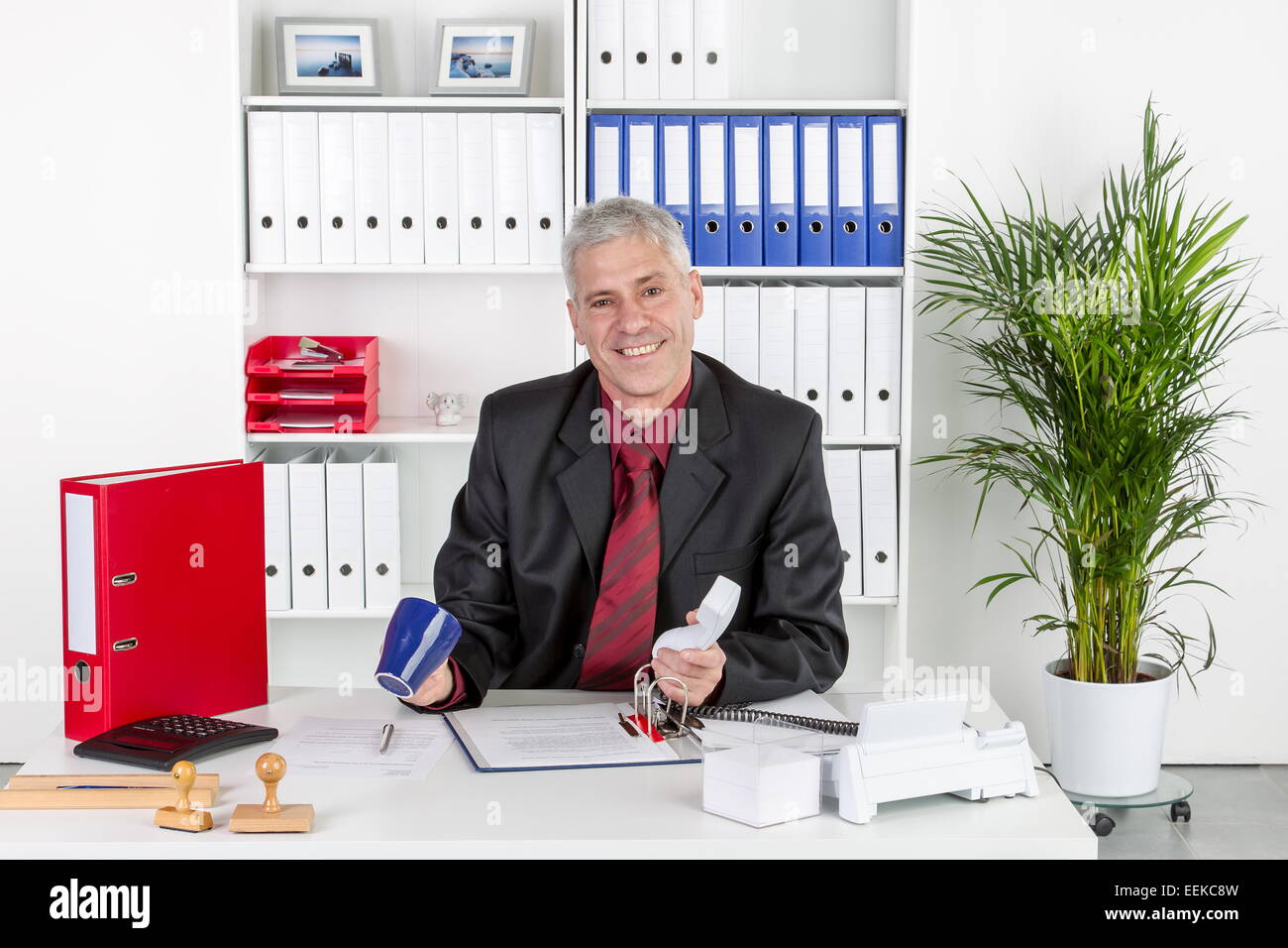 Mann mittleren Alters sitzt im Büro am Schreibtisch mit leerer Tasse Kaffee in der Hand, Middle-aged man sits in an office Stock Photo