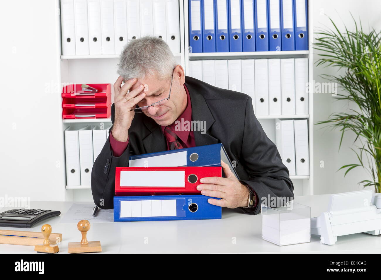 Mann mittleren Alters sitzt im Büro, hält sich den Kopf, hat Kopfschmerzen, Middle-aged man with a headache, sits in his office, Stock Photo