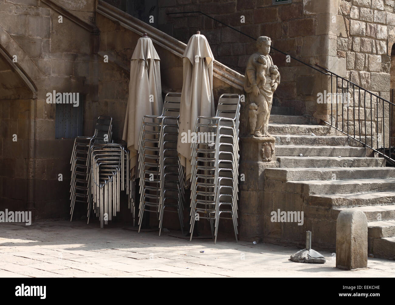 Statue and steps beside stacked chairs and folded umbrellas in gardens of the old Hospital de la Santa Creu, El Raval, Barcelona Stock Photo