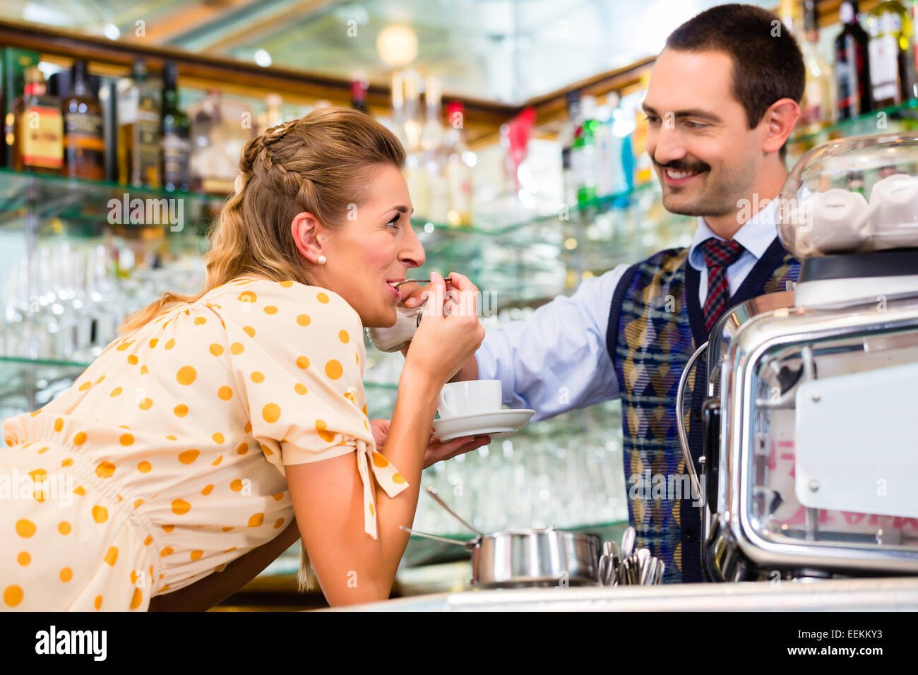 Girl in cafe or coffee bar flirting with barista who is busy preparing Cappuccino with professional machine Stock Photo
