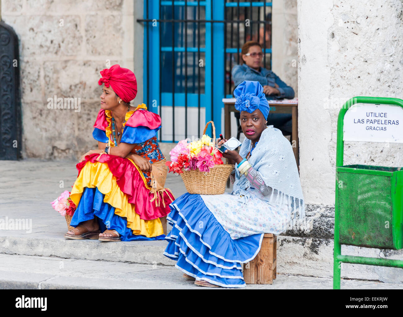 View of local women dressed in brightly coloured traditional dresses for tips selling flowers in Cathedral Square, Old Havana, Cuba, applying lipstick Stock Photo