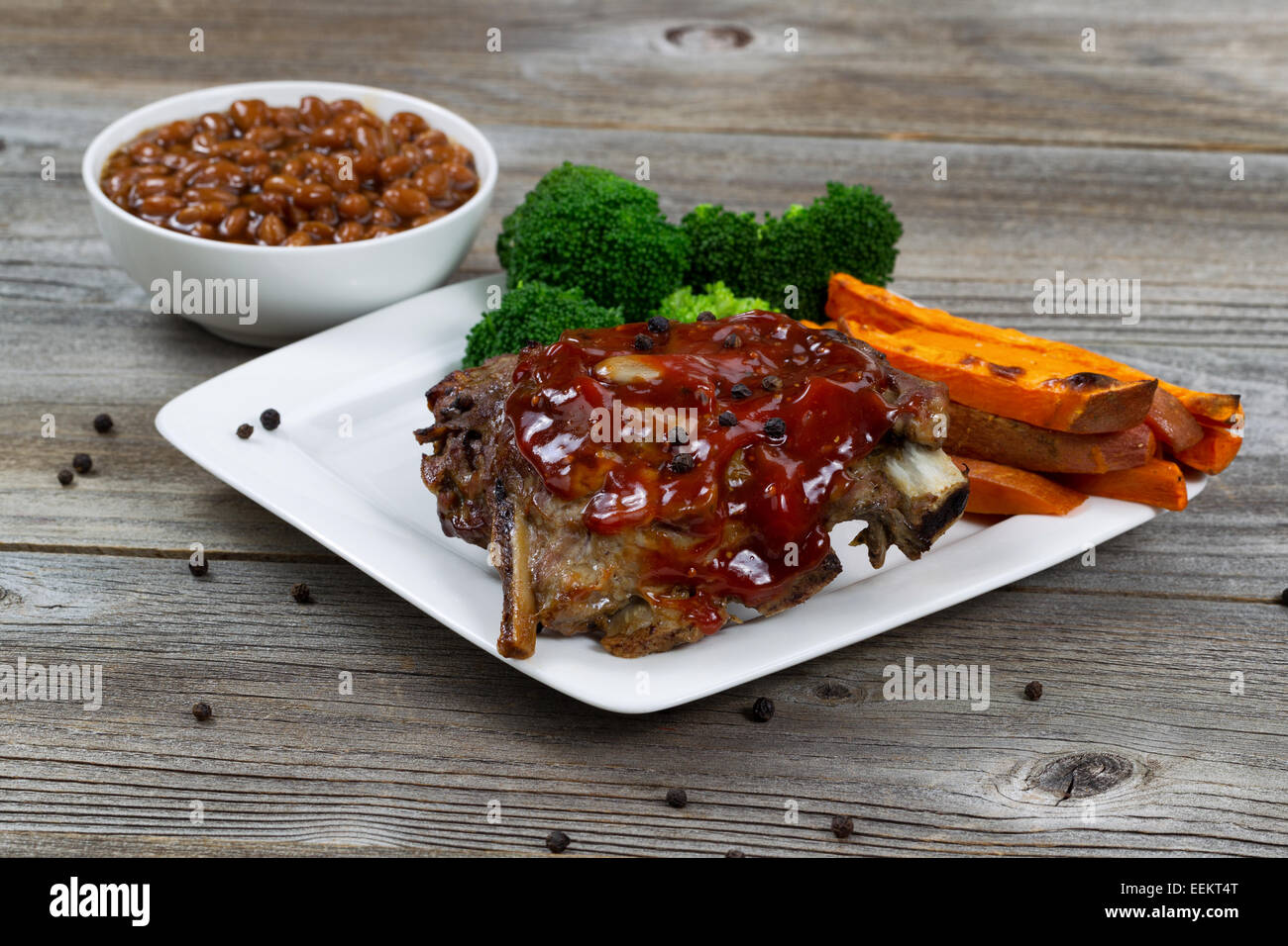 Barbecued spare ribs with yam French fries, broccoli and baked beans on rustic wooden table. Stock Photo