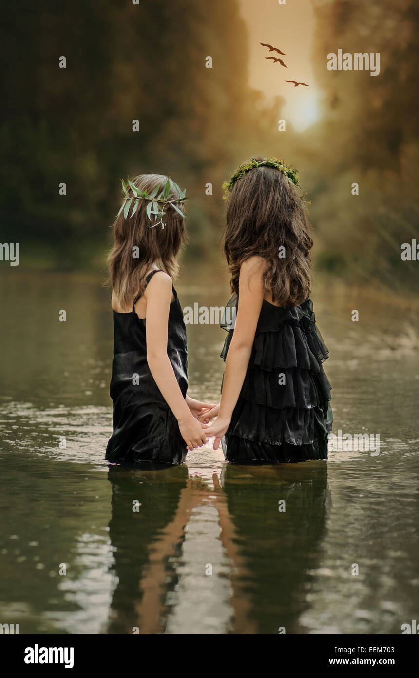 Two girls (8-9, 10-11) holding hands and watching sunset Stock Photo