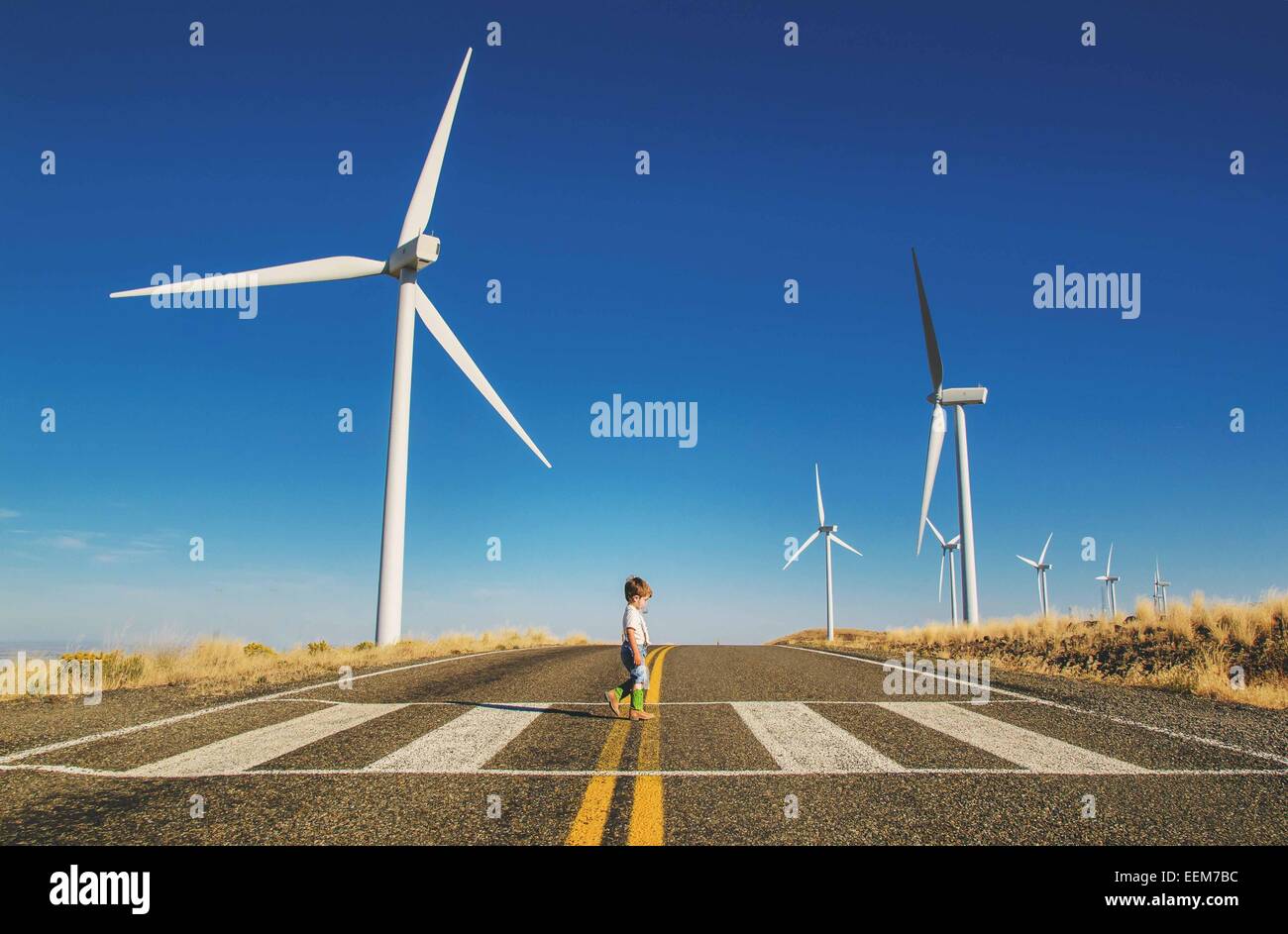 Boy crossing a road near a wind farm, USA Stock Photo