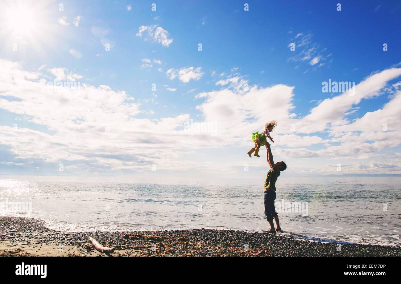 Father standing on beach throwing his daughter in the air, USA Stock Photo