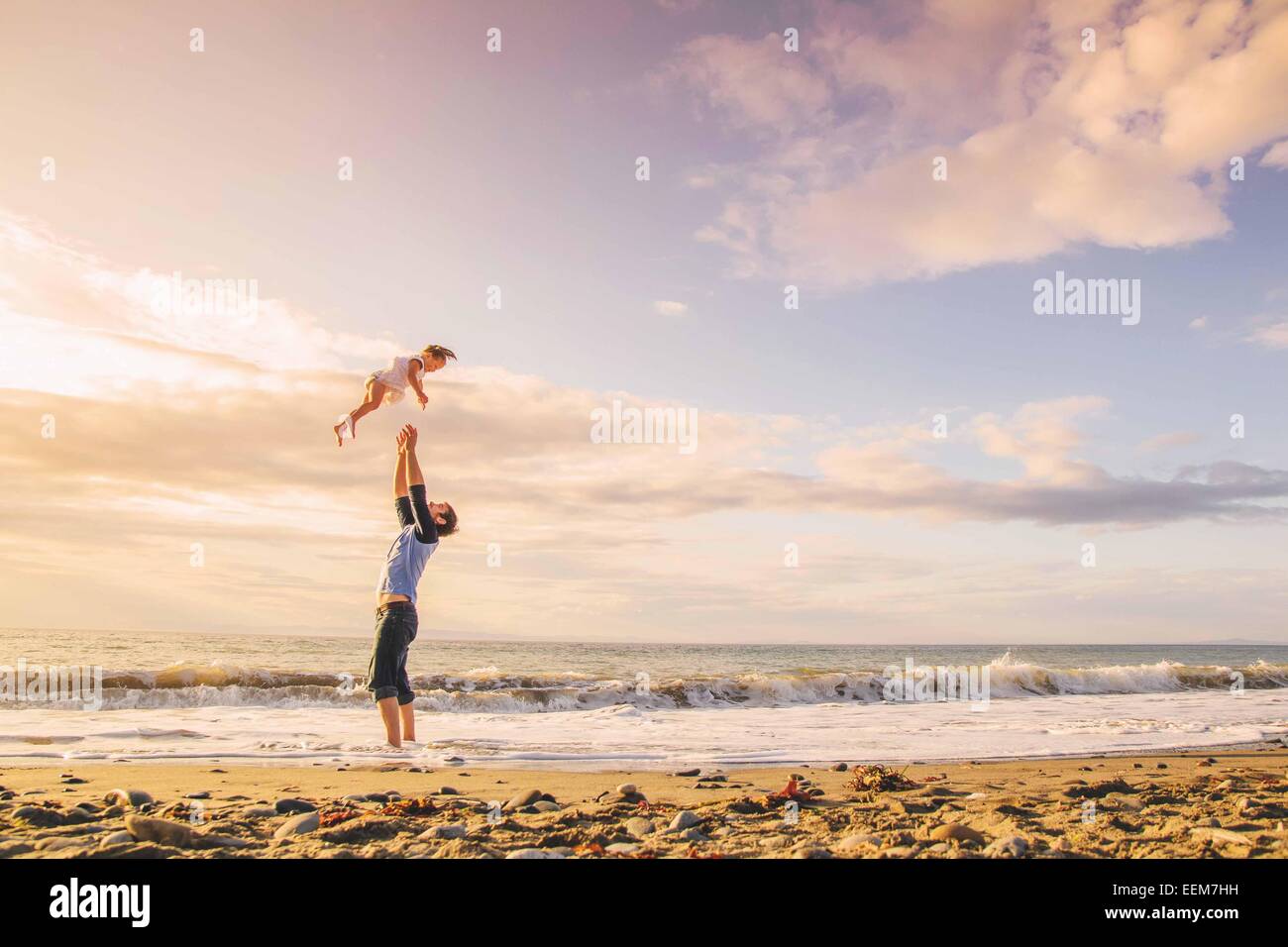 Father standing on beach throwing his daughter in the air, USA Stock Photo